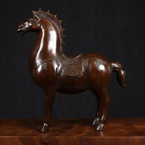 May include: A bronze sculpture of a horse with a saddle and intricate details. The horse is standing on a wooden base.