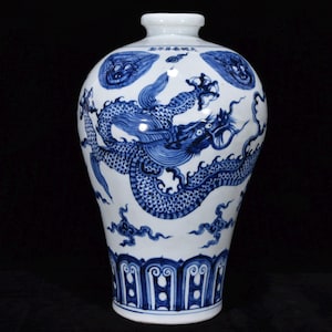 Op de afbeelding: Een witte porseleinen vaas met handgeschilderde blauwe onderglazuurontwerpen van een grote draak, wervelende wolken en gestileerde bloemmotieven. De hals van de vaas toont een horizontale lijn met Chinese karakters in blauwe inkt.