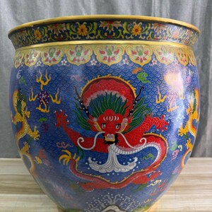 Peut inclure: Un grand vase décoratif rond bleu avec un motif de dragon détaillé. Le vase présente un dragon rouge au centre, avec des dragons dorés et jaunes sur les côtés. Le bord est doré avec des motifs floraux.