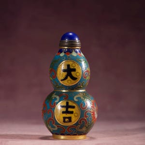 Puede incluir: Una botella decorativa en forma de doble calabaza con tapón azul. La botella presenta un fondo turquesa con patrones florales rojos, verdes y dorados. Círculos dorados con caracteres chinos negros están centrados en la botella. La botella mide unos 10 cm de altura.