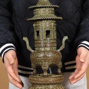 Op de afbeelding: Bronzen wierookbrander in pagodestijl met ingewikkelde details. De brander heeft meerdere niveaus, decoratieve patronen en gebogen handvatten. De basis is een ronde sokkel met een gedetailleerd ontwerp. De totale hoogte is ongeveer 30 cm.