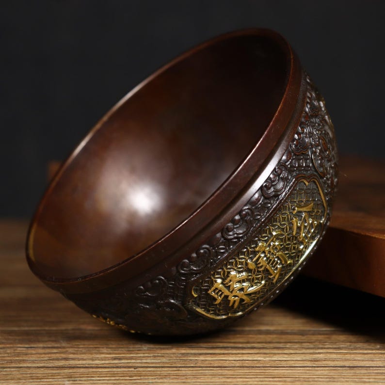 May include: A brown bronze bowl with intricate gold detailing and Chinese characters. The bowl is sitting on a wooden surface.