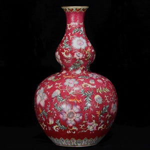 May include: A red double gourd vase with floral patterns. The vase has a vibrant red background with detailed illustrations of flowers, leaves, and vines in various colours. The rim has a gold trim.