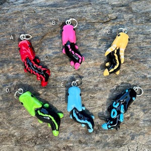 Könnte beinhalten: Eine Sammlung von sechs farbenfrohen, handgefertigten Polymer-Ton-Anhängern. Jeder Anhänger hat ein einzigartiges Design mit leuchtenden Farben wie Rot, Pink, Gelb, Grün, Blau und Schwarz, mit einer silberfarbenen Metallschlaufe.