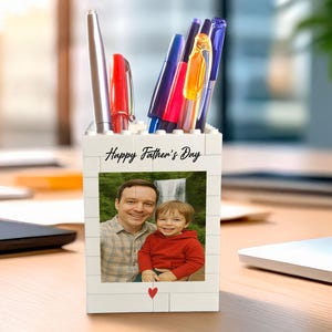 Könnte beinhalten: Ein weißer Stifthalter im Ziegelstil mit einem Foto eines Mannes und eines Kindes und dem Text "Happy Father's Day". Der Halter enthält Stifte und Bleistifte in verschiedenen Farben. Unter dem Foto befindet sich ein rotes Herz.