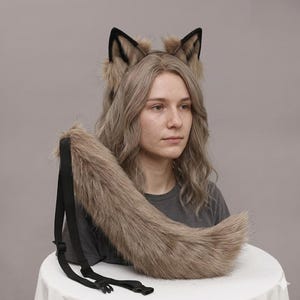 May include: A faux fur wolf tail and ear set. The ears are black-tipped and attached to a headband. The tail is a light brown color and has a black adjustable strap. The set is designed for cosplay or costume use.