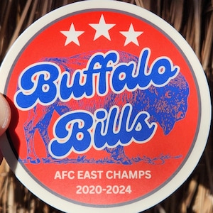 May include: A red and white circular sticker with a blue buffalo silhouette and the text "Buffalo Bills" in a blue, cursive font. The sticker also includes three white stars and the text "AFC East Champs 2020-2024".