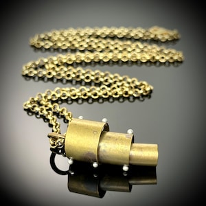 May include: A gold necklace with a unique pendant made of stacked brass cylinders. The pendant has a textured surface and is accented with small silver beads.