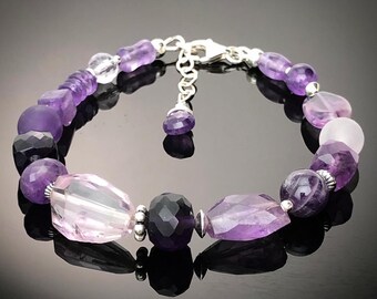 May include: A purple and pink gemstone bracelet with a silver clasp. The bracelet features a variety of amethyst and rose quartz beads.