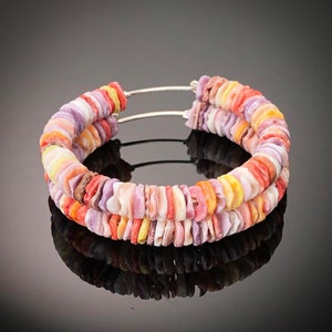 May include: A pair of hoop earrings made of colorful, layered, and polished shell pieces. The earrings are connected by a silver wire.