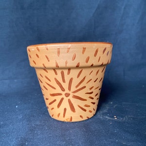 May include: A terracotta flower pot with a brown geometric design. The pot is painted with a pattern of radiating lines.