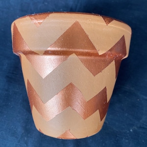 May include: A terracotta flower pot with a chevron pattern painted in copper and tan.