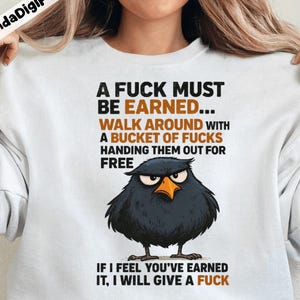 May include: White sweatshirt with the text "A FUCK MUST BE EARNED... WALK AROUND WITH A BUCKET OF FUCKS HANDING THEM OUT FOR FREE. IF I FEEL YOU'VE EARNED IT, I WILL GIVE A FUCK." Features a cartoon black bird with an angry expression.