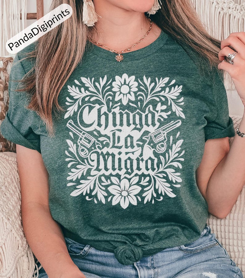May include: Green t-shirt featuring a white floral design and the text "Chinga La Migra". The design includes two revolvers. The shirt is made of a soft material.