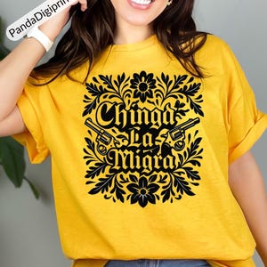May include: A yellow t-shirt featuring a black floral design with the text "Chinga La Migra" and two guns. The shirt is made of a soft material and has short sleeves.