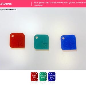 May include: Three square acrylic pieces in ruby red, emerald green, and sapphire blue with silver glitter. Each piece features a circular hole in the top left corner and a small embossed square icon in the bottom right corner. Text reads Gemstones.