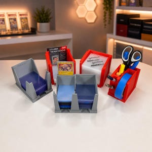 May include: A collection of 3D-printed plastic organizers for trading cards and supplies. The set includes gray and red open-top bins holding card sleeves, a pack of Ultra-PRO Team Bags, a single trading card, and a red caddy containing scissors and tape.