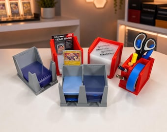 May include: A collection of red and gray plastic organizers for trading cards and supplies. The set includes open-top bins holding card sleeves, a pack of Ultra-PRO Team Bags, a single trading card, and a red caddy containing scissors and tape.