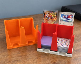 May include: Two plastic trading card organizers with two slots each. One is orange, and the other is red with a white base. The red organizer holds stacks of cards in protective sleeves, including a Skarmory card. Both feature the word Sleeves.