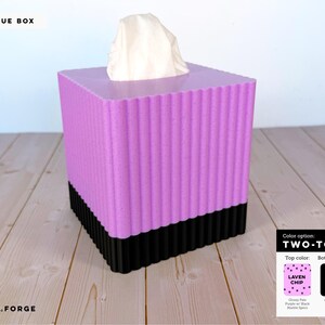 May include: A square tissue box with a fluted, vertical ribbed texture. The top section is a speckled lavender color, while the bottom section is solid black. A white tissue protrudes from the top opening. A color chart label indicates the top color as Laven Chip and the bottom as black.