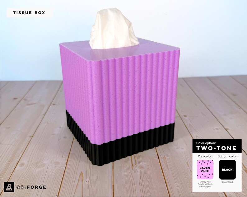 May include: A square tissue box with a fluted, vertical ribbed texture. The top section is a speckled lavender color, while the bottom section is solid black. A white tissue protrudes from the top opening. A color chart label indicates the top color as Laven Chip and the bottom as black.