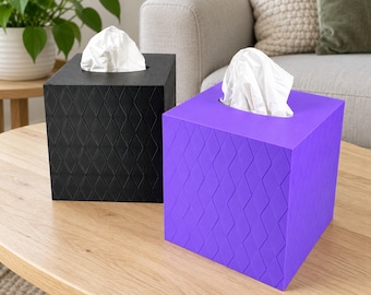 May include: Two square tissue box covers, one black and one purple, each featuring a raised diamond pattern on the exterior. Both boxes are open at the top, with white tissues protruding from the center of each container.