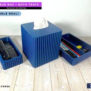 May include: A navy blue ribbed tissue box cover with a white tissue protruding from the top, accompanied by two matching navy blue ribbed rectangular trays. One tray holds a black remote control, and the other holds several pens and markers.