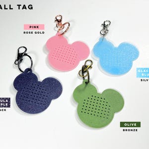 May include: Four small mouse-shaped tags with metal lobster clasps. Colors include nebula purple with black hardware, pink with rose gold hardware, glacier blue with silver hardware, and olive with bronze hardware. Each tag features a grid of small holes.