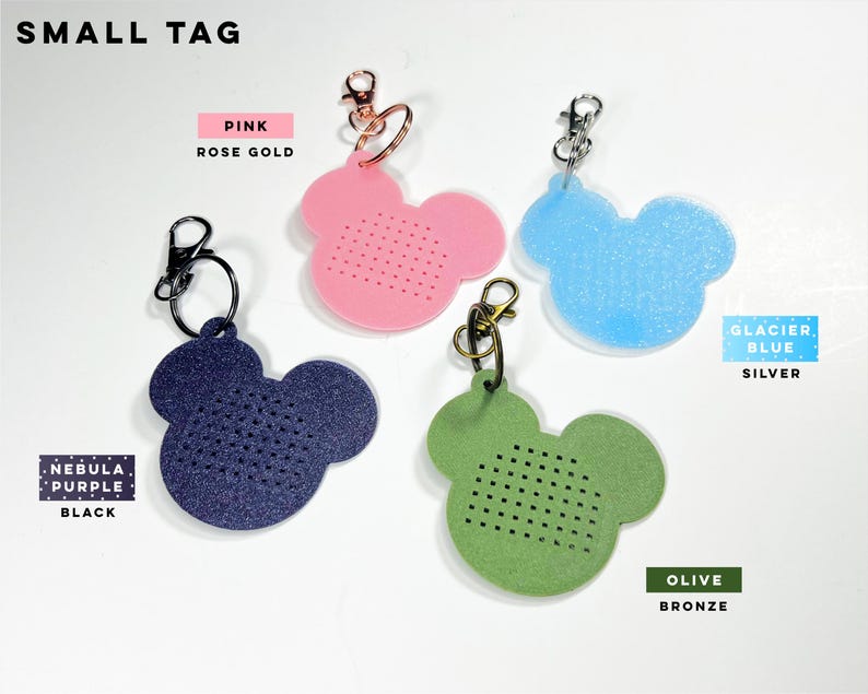 May include: Four small mouse-shaped tags with metal lobster clasps. Colors include nebula purple with black hardware, pink with rose gold hardware, glacier blue with silver hardware, and olive with bronze hardware. Each tag features a grid of small holes.
