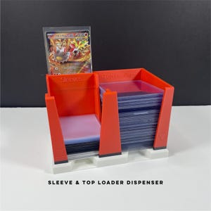 May include: An orange and white plastic sleeve and top loader dispenser. The dispenser holds a stack of clear card sleeves and top loaders. A trading card is displayed in a sleeve. The text "Sleeve & Top Loader Dispenser" is printed on the base.