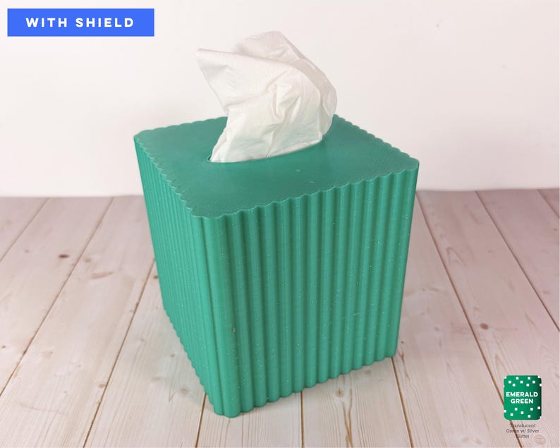 May include: A square emerald green tissue box cover with a vertical ribbed texture and a scalloped top edge. A white tissue protrudes from the center opening. The text WITH SHIELD appears in the top left, and EMERALD GREEN is in the bottom right.