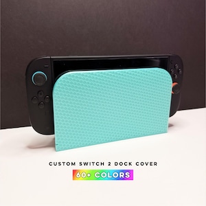 May include: A black Nintendo Switch console docked with a teal honeycomb-patterned cover. The cover has a curved design and the text "CUSTOM SWITCH 2 DOCK COVER" and "60+ COLORS" in a rainbow gradient.