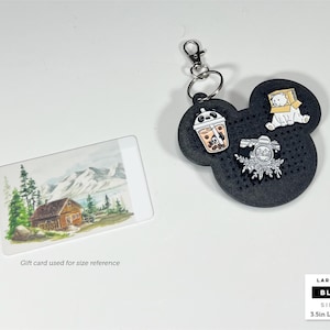 May include: A black, mouse-shaped pin display board with a silver keychain, featuring three enamel pins: a panda boba tea, a white bear in a box, and a floral camera. The tag measures 3.5 inches long by 3.2 inches wide, shown with a gift card.