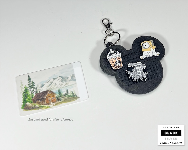 May include: A black, mouse-shaped pin display board with a silver keychain, featuring three enamel pins: a panda boba tea, a white bear in a box, and a floral camera. The tag measures 3.5 inches long by 3.2 inches wide, shown with a gift card.