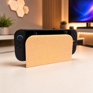 May include: A black gaming console dock featuring a light orange front panel with a repeating hexagonal honeycomb pattern. The console is equipped with two black controllers, one with a blue joystick and the other with a red joystick.