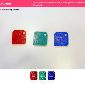 May include: Three square-shaped plastic tiles in red, green, and blue, each featuring a textured surface with silver glitter and a small circular hole in the top right corner. Text on the image includes Gemstones, Build Plate Side, Ruby Red, Emerald Green, and Sapphire Blue.