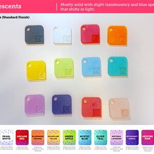 May include: A collection of twelve square-shaped swatches with rounded corners and a circular hole in the top left corner. The swatches are arranged in three rows and feature various colors including black, white, red, orange, yellow, green, blue, teal, lavender, purple, and pink.