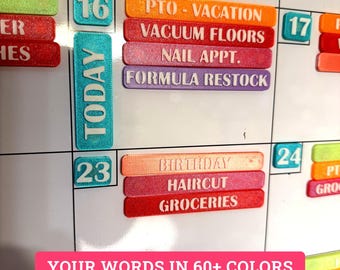 Könnte beinhalten: Ein Set aus 3D-gedruckten magnetischen Kalenderetiketten in verschiedenen Farben mit geprägtem Text wie PTO - VACATION, VACUUM FLOORS, NAIL APPT., FORMULA RESTOCK, BIRTHDAY, HAIRCUT und GROCERIES auf einem weißen magnetischen Whiteboard.