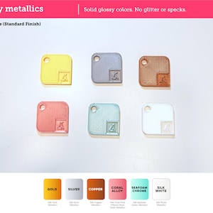 May include: Six square tags with rounded corners and a circular hole, featuring a silky metallic finish in gold, silver, copper, coral alloy, seafoam chrome, and white. Each tag displays a small embossed logo in the bottom right corner.