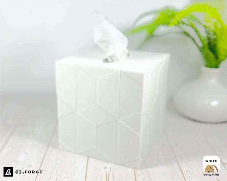 Pu&ograve; includere: Un copriscatola per fazzoletti quadrato di colore bianco lucido con un motivo geometrico sfaccettato sulle superfici esterne. Un fazzoletto bianco sporge dall'apertura rettangolare sulla parte superiore. Il testo CD.FORGE &egrave; visibile nell'angolo.