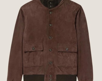 May include: A brown suede bomber jacket with a dark brown ribbed collar, cuffs, and hem. The jacket features two front pockets with button closures and a button-up front. The jacket has a classic, timeless design.