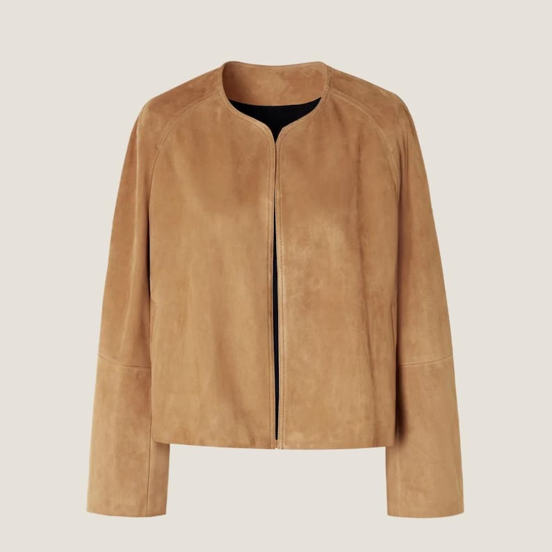 Puede incluir: Chaqueta de ante color canela sin cuello y con mangas largas. La chaqueta tiene una est&eacute;tica limpia y minimalista, con un dobladillo recto y una parte delantera abierta y sencilla. El interior es negro.