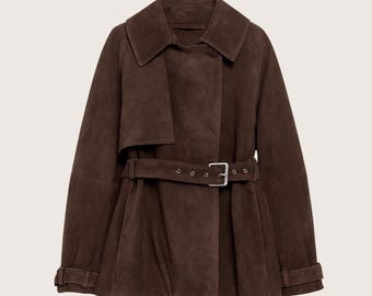 Op de afbeelding: Een donkerbruine suède trenchcoat met een brede kraag en een dubbele rij knopen. Het heeft een riem in de taille en lange mouwen met manchetten met knopen. De jas heeft een klepdetail op de rechterschouder.