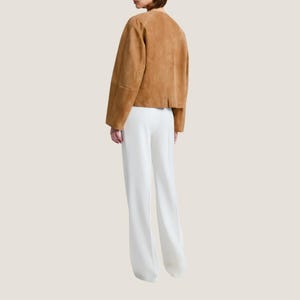 Puede incluir: Una chaqueta de ante marr&oacute;n claro con cuello redondo y mangas largas se combina con pantalones blancos de pernera ancha. La chaqueta tiene un corte corto y los pantalones tienen cintura alta. El conjunto es sencillo y elegante, adecuado para diversas ocasiones.