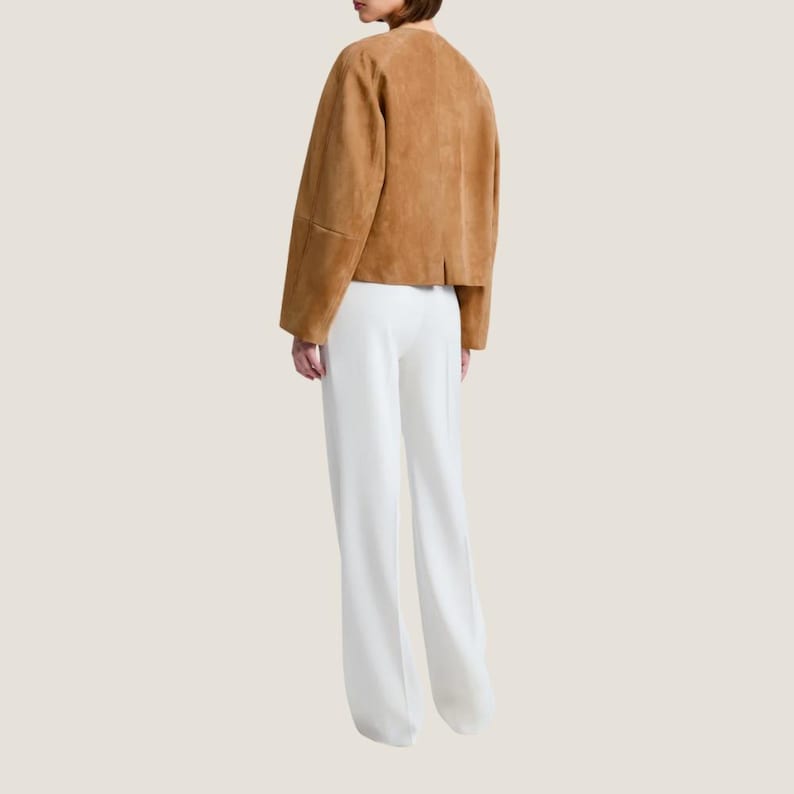Puede incluir: Una chaqueta de ante marr&oacute;n claro con cuello redondo y mangas largas se combina con pantalones blancos de pernera ancha. La chaqueta tiene un corte corto y los pantalones tienen cintura alta. El conjunto es sencillo y elegante, adecuado para diversas ocasiones.