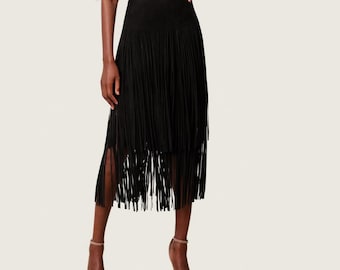 May include: A black midi skirt with long fringe detailing. The skirt has a high waist and falls to the mid-calf, with fringe that moves with the wearer. The skirt is paired with a white button-down shirt and neutral heels.