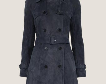 May include: A navy blue suede trench coat with a double-breasted design. The coat features a belt at the waist, epaulets on the shoulders, and buttoned cuffs. The coat is approximately knee-length.
