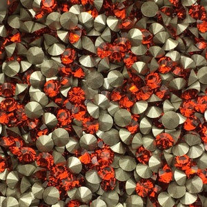 May include: A close-up of a bowl filled with a mixture of silver and orange rhinestones. The rhinestones are arranged in a random pattern.