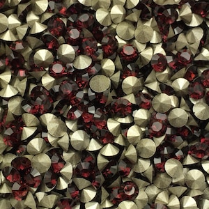 Könnte beinhalten: Nahaufnahme eines Behälters gefüllt mit einer Mischung aus silbernen und burgunderfarbenen Strasssteinen. Die Strasssteine sind klein und haben eine spitze Form.