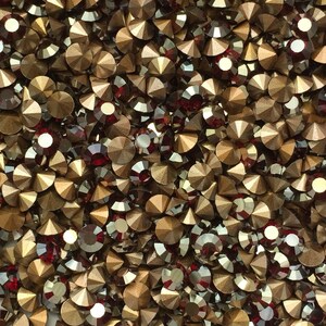 Könnte beinhalten: Nahaufnahme einer Schale gefüllt mit kleinen, runden, schillernden Strasssteinen. Die Strasssteine sind eine Mischung aus Gold und Rot.